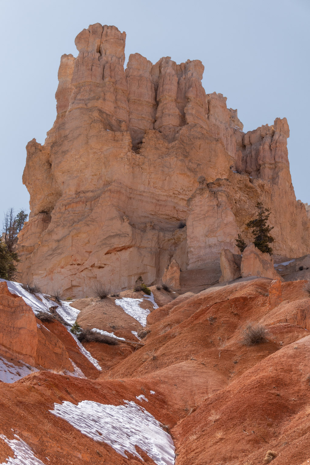 Light orange hoodoos rise above more saturated rolling sort of cliffs with a light blue sky